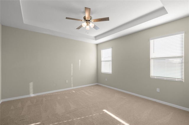 spare room featuring light carpet, baseboards, a raised ceiling, and a ceiling fan