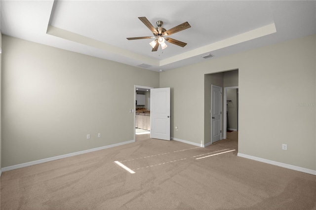 unfurnished bedroom featuring visible vents, baseboards, a tray ceiling, ceiling fan, and light carpet