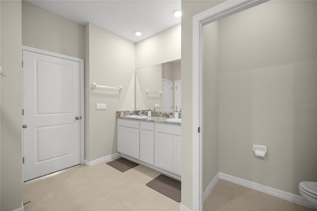 bathroom with toilet, a sink, tile patterned flooring, double vanity, and baseboards