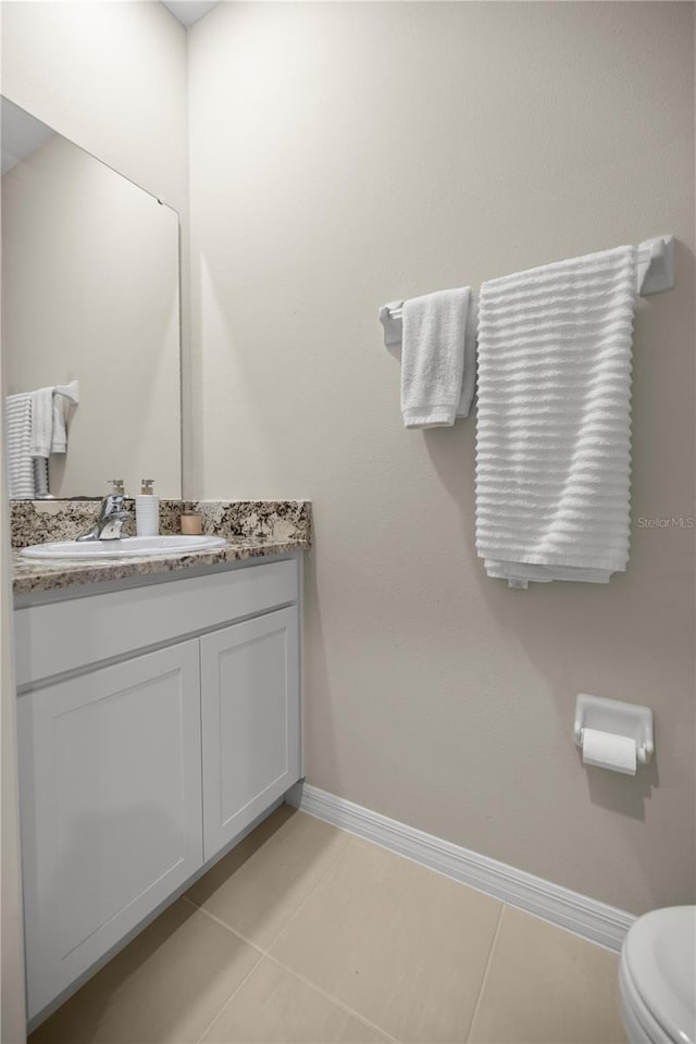 half bath featuring tile patterned floors, toilet, vanity, and baseboards