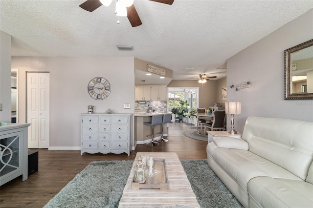 living area featuring baseboards, visible vents, dark wood-style flooring, and a textured ceiling