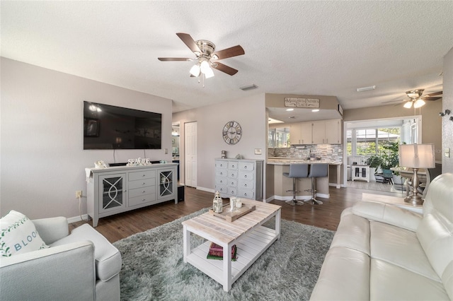 living area with a textured ceiling, baseboards, ceiling fan, and wood finished floors