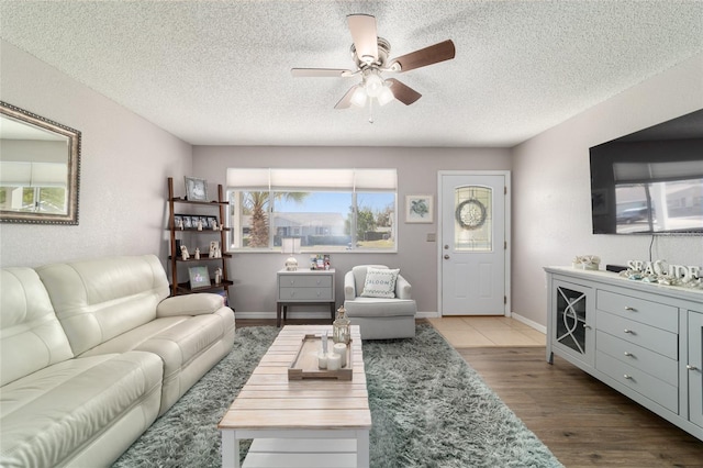 living area featuring baseboards, a textured ceiling, a ceiling fan, and wood finished floors