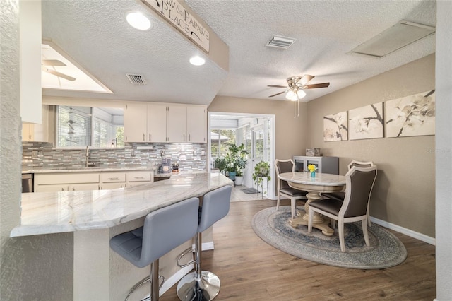 kitchen featuring visible vents, wood finished floors, decorative backsplash, and white cabinetry