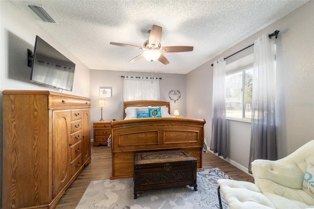 bedroom featuring a ceiling fan, wood finished floors, visible vents, and a textured ceiling