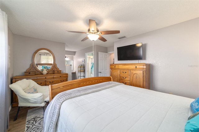 bedroom with ceiling fan, wood finished floors, visible vents, and a textured ceiling