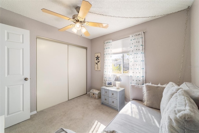 bedroom featuring a closet, light colored carpet, a textured ceiling, and ceiling fan