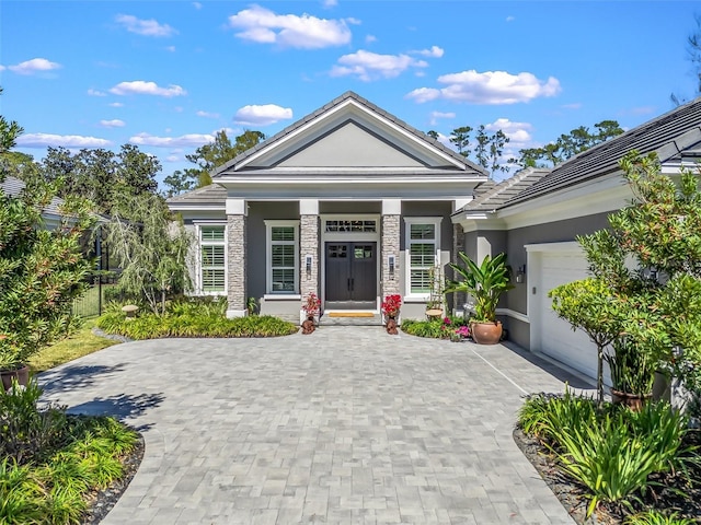 neoclassical / greek revival house with stone siding, a garage, decorative driveway, and stucco siding