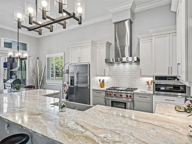 kitchen featuring ornamental molding, stainless steel appliances, wall chimney range hood, tasteful backsplash, and a chandelier