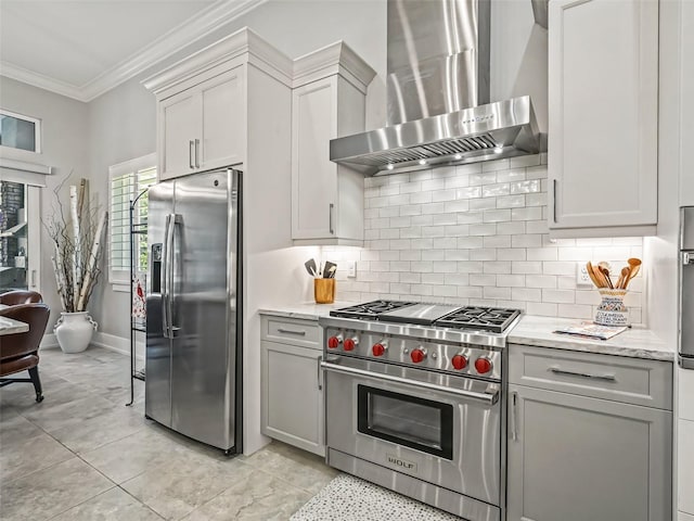 kitchen with gray cabinets, decorative backsplash, appliances with stainless steel finishes, crown molding, and wall chimney exhaust hood