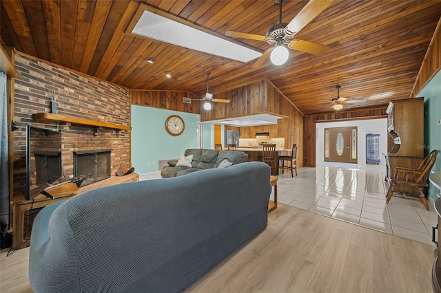 living area with lofted ceiling with skylight, wood walls, wood ceiling, light wood-style flooring, and a fireplace