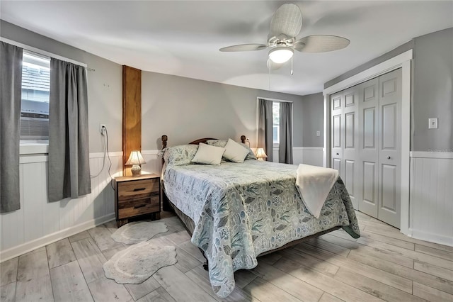 bedroom featuring light wood finished floors, wainscoting, a ceiling fan, and a closet