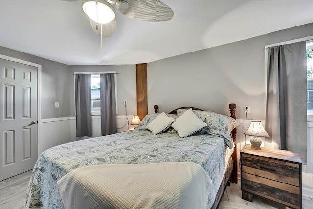 bedroom featuring a wainscoted wall, light wood-style floors, and a ceiling fan