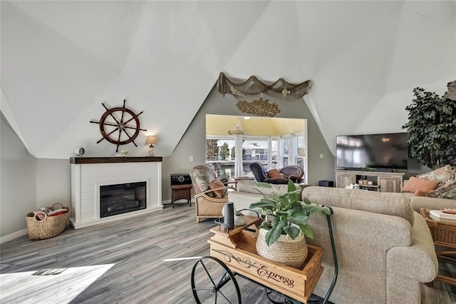 living room featuring baseboards, light wood finished floors, a glass covered fireplace, and vaulted ceiling