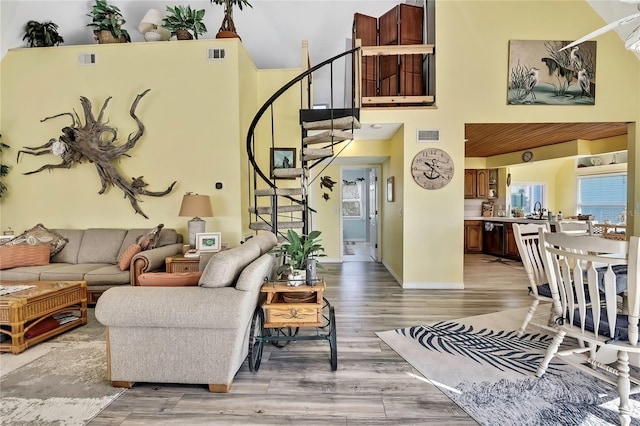 living area featuring a high ceiling, stairway, light wood-style floors, and visible vents