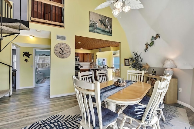 dining space featuring a ceiling fan, visible vents, baseboards, a towering ceiling, and light wood-type flooring