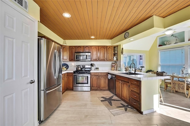 kitchen featuring a sink, open shelves, appliances with stainless steel finishes, a peninsula, and brown cabinetry