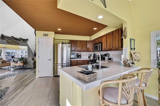 kitchen featuring tile countertops, visible vents, a peninsula, stainless steel appliances, and light wood-type flooring