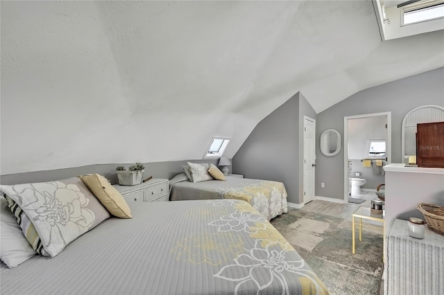 bedroom featuring wood finished floors, baseboards, lofted ceiling with skylight, and ensuite bath