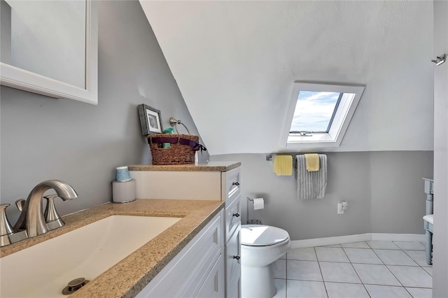 bathroom featuring vanity, baseboards, vaulted ceiling with skylight, tile patterned floors, and toilet