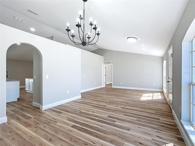 spare room featuring lofted ceiling, light wood-style flooring, visible vents, and arched walkways