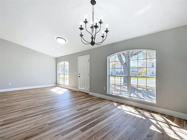 empty room with wood finished floors, baseboards, and an inviting chandelier