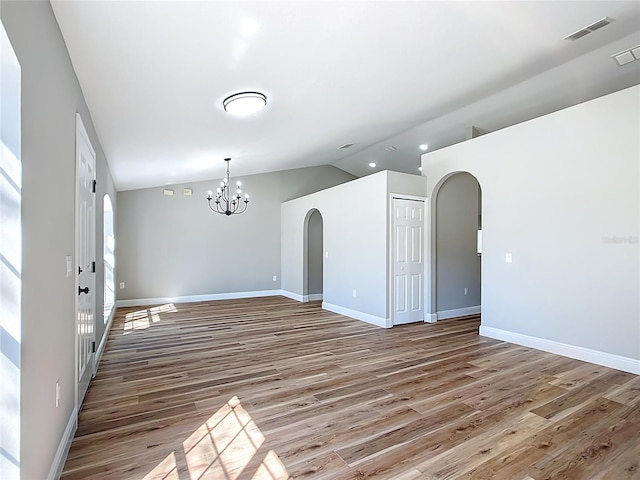 spare room with arched walkways, baseboards, vaulted ceiling, light wood-style floors, and an inviting chandelier