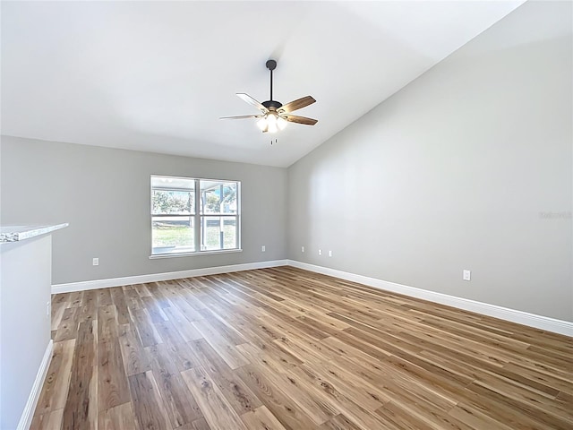 unfurnished room featuring a ceiling fan, vaulted ceiling, baseboards, and wood finished floors