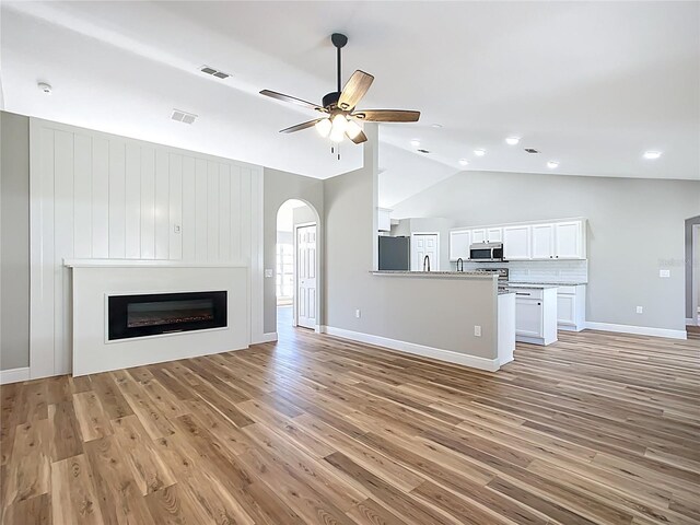 unfurnished living room with lofted ceiling, light wood-type flooring, visible vents, and arched walkways