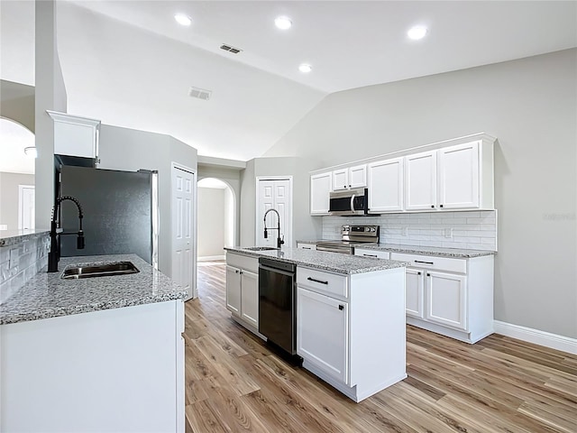 kitchen with arched walkways, stainless steel appliances, lofted ceiling, visible vents, and a sink