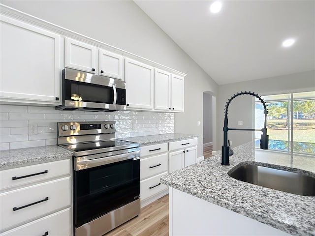 kitchen featuring tasteful backsplash, lofted ceiling, appliances with stainless steel finishes, white cabinetry, and a sink