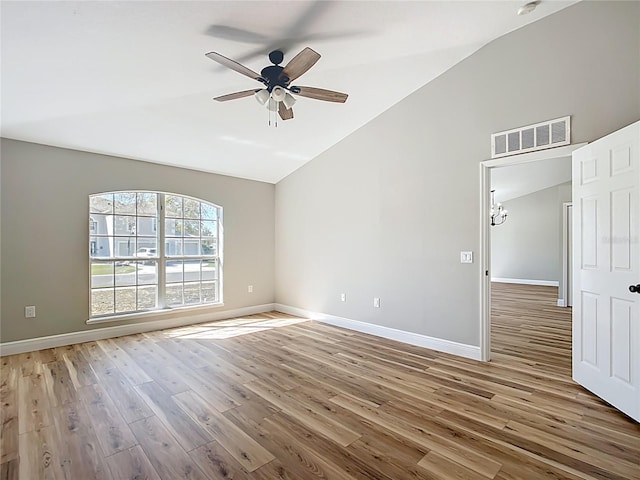 empty room with lofted ceiling, visible vents, a ceiling fan, wood finished floors, and baseboards