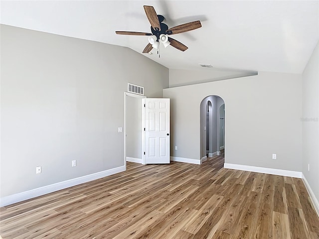 empty room featuring vaulted ceiling, visible vents, arched walkways, and wood finished floors