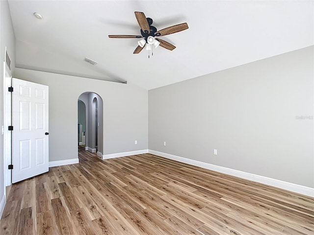 spare room with arched walkways, lofted ceiling, a ceiling fan, light wood-type flooring, and baseboards