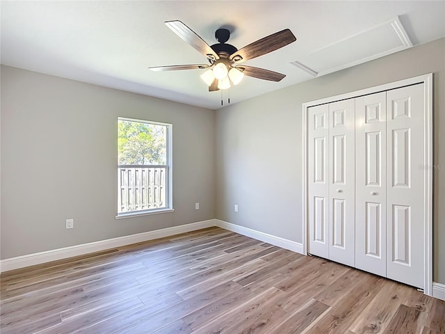 unfurnished bedroom with ceiling fan, baseboards, a closet, light wood finished floors, and attic access