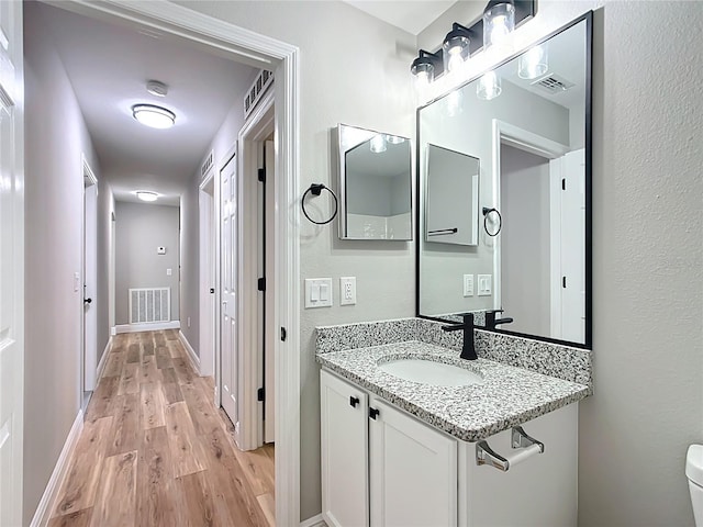 half bathroom with visible vents, vanity, baseboards, and wood finished floors