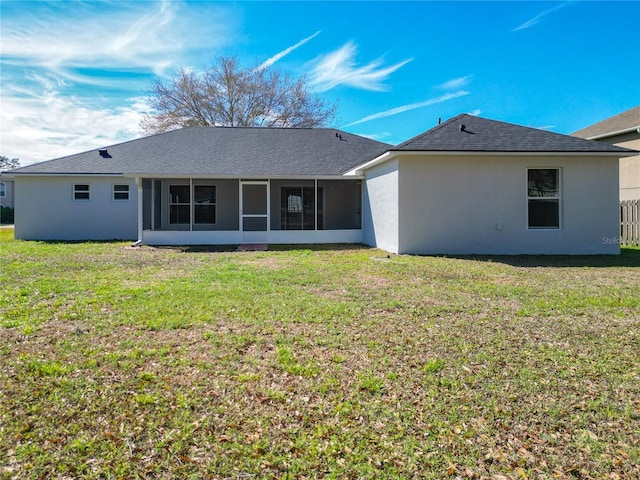 back of property with a sunroom, roof with shingles, a lawn, and stucco siding