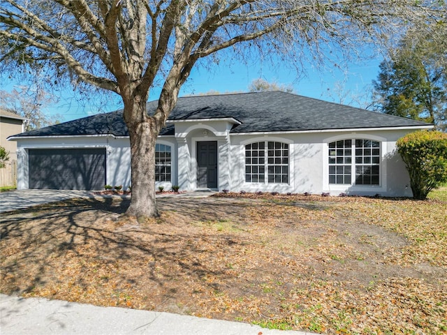 ranch-style home featuring a shingled roof, concrete driveway, an attached garage, and stucco siding