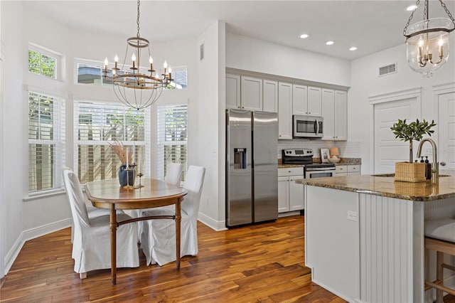 kitchen with dark wood-style flooring, a notable chandelier, stainless steel appliances, visible vents, and decorative backsplash