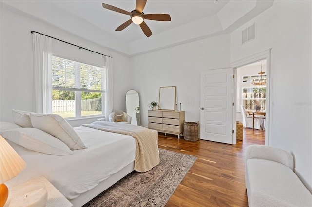 bedroom featuring ceiling fan, visible vents, a raised ceiling, and wood finished floors