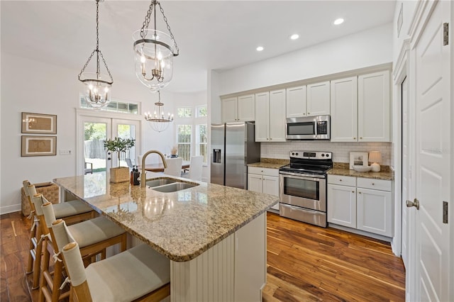 kitchen featuring stainless steel appliances, backsplash, a sink, a breakfast bar area, and a notable chandelier