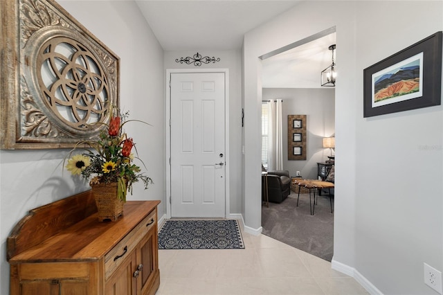 foyer featuring light carpet, an inviting chandelier, baseboards, and light tile patterned flooring