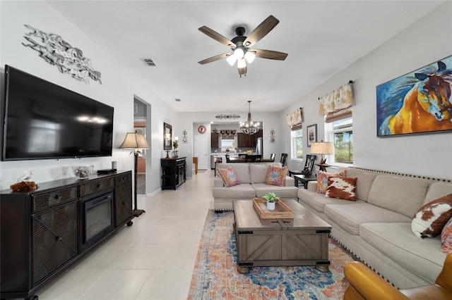 living room with light tile patterned floors, visible vents, ceiling fan with notable chandelier, and a glass covered fireplace