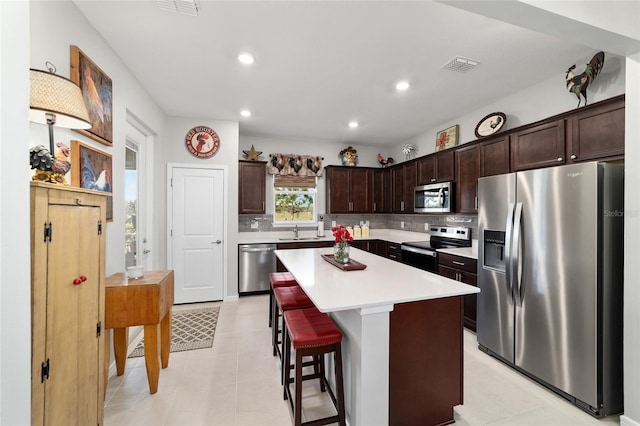 kitchen with visible vents, dark brown cabinets, a center island, decorative backsplash, and stainless steel appliances