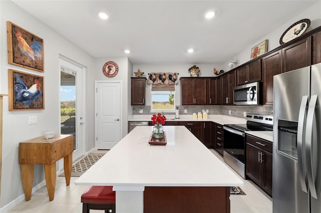 kitchen featuring a breakfast bar area, stainless steel appliances, light countertops, dark brown cabinetry, and tasteful backsplash