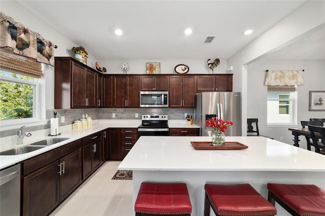 kitchen featuring backsplash, a kitchen bar, light countertops, stainless steel appliances, and a sink