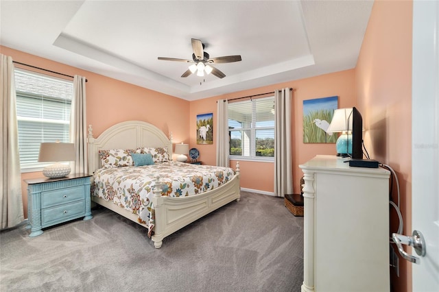 carpeted bedroom featuring a tray ceiling, a ceiling fan, and baseboards