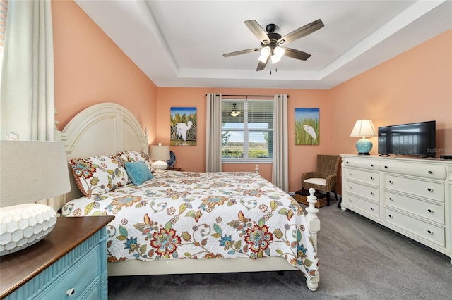 bedroom featuring a ceiling fan, a tray ceiling, and dark colored carpet