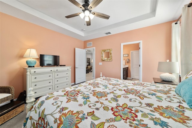 carpeted bedroom featuring visible vents, a raised ceiling, ensuite bath, and a ceiling fan