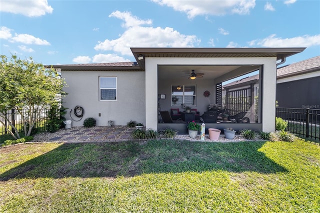 back of property with stucco siding, a ceiling fan, a yard, and fence